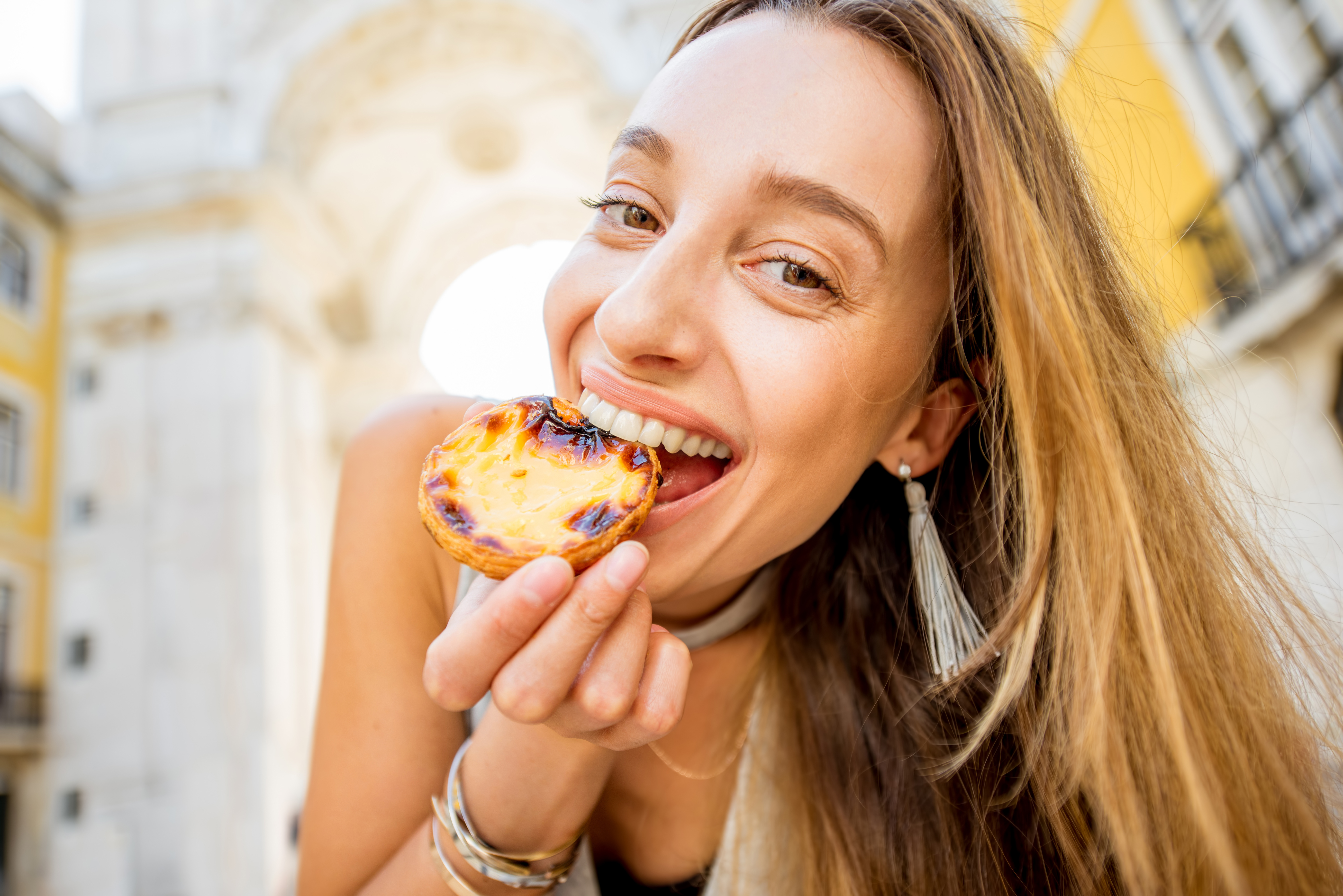 Young woman holding portuguese egg tart pastry called pastel de Nata outdoors on the triumphal arch background in Lisbon